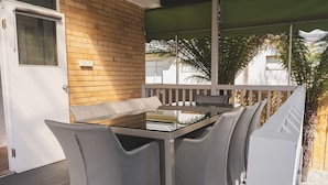Eine Terrasse mit Glastisch und gepolsterten Stühlen, einer Ziegelwand und einem Holzboden.