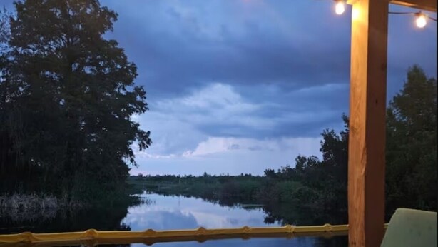 An outdoor deck with a view of a calm body of water, surrounded by trees and a wooden structure. - Cozy RV off the Withlacoochee River (Dunnellon)