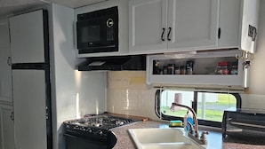 A compact RV kitchen with a stove, sink, microwave, and storage cabinets. - Cozy RV off the Withlacoochee River (Dunnellon)