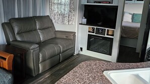 A compact RV interior with a sofa, kitchenette, and a small bed. - Cozy RV off the Withlacoochee River (Dunnellon)
