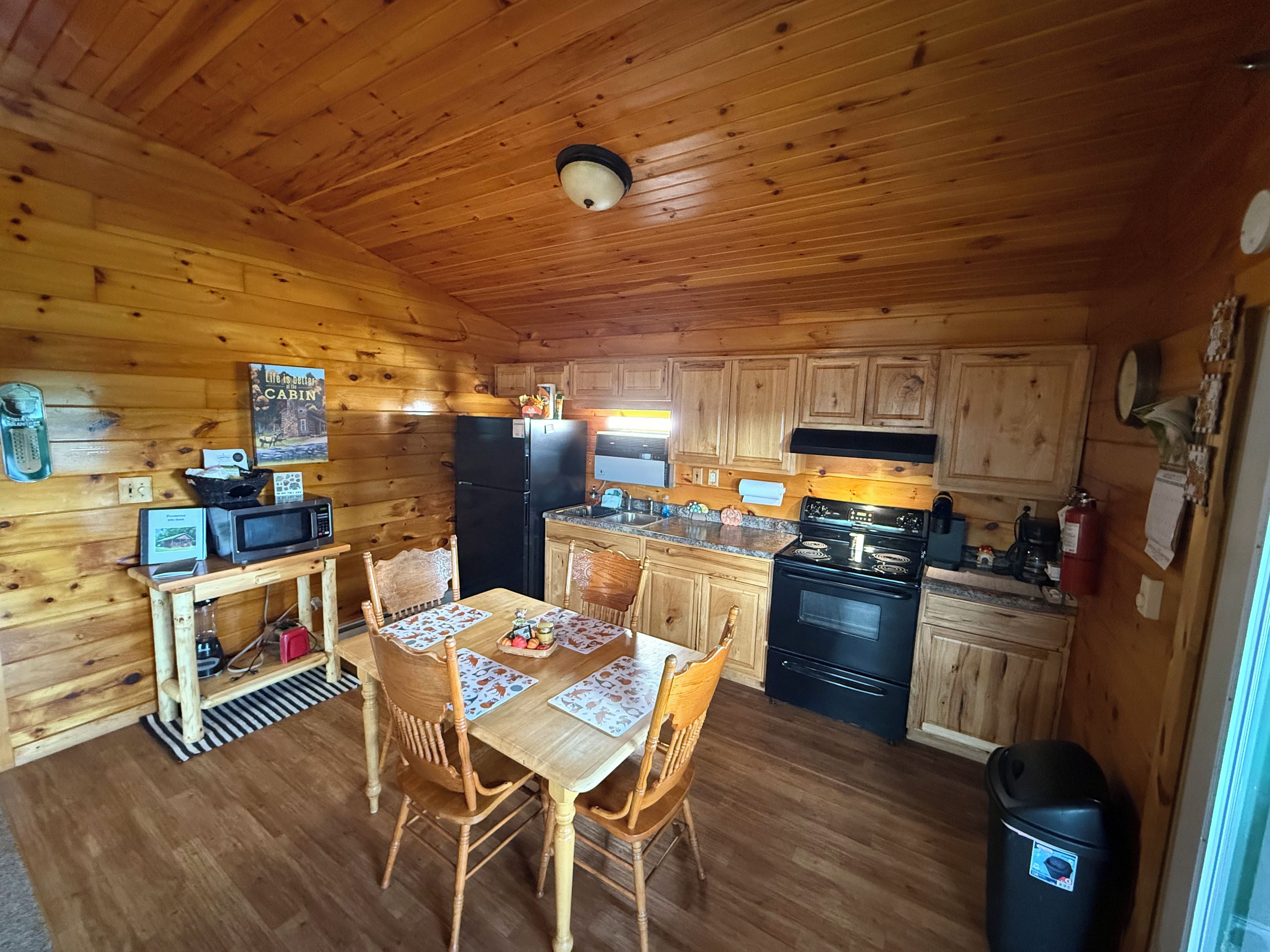 A wooden cabin interior with a dining table, chairs, a refrigerator, a stove, and a microwave.