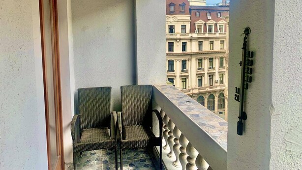 A balcony with wicker chairs and a small table, overlooking a building with classical architecture. - Belgrade heart of historical center (Belgrade)