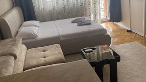 A modern bedroom with a bed, a sofa, a TV, and a small table with remote controls. - APARTMENT PERLA (Pristina)