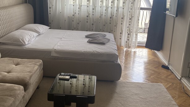 A bedroom with a bed, a sofa, a TV, and a window with curtains. - APARTMENT PERLA (Pristina)