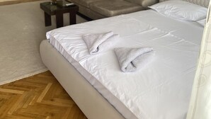 A bedroom with a bed, a sofa, a small table, and a painting on the wall. - APARTMENT PERLA (Pristina)