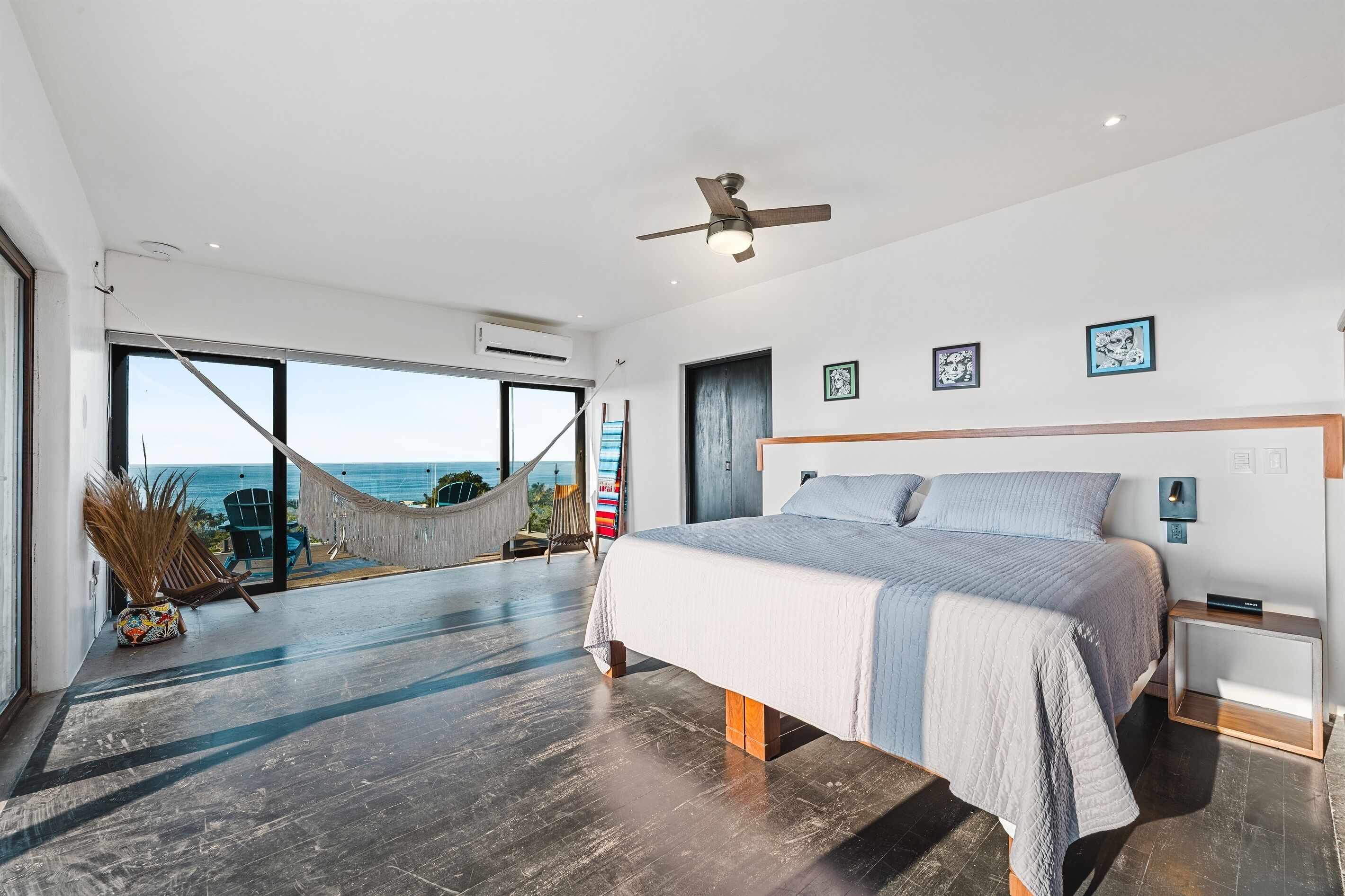 Un dormitorio moderno con una cama grande, un ventilador de techo y vista al océano a través de un ventanal.