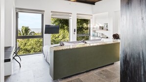A modern kitchen with a large island, a dining area with a bench, and a view of greenery outside. - Stunning Ocean Views; 2 Pools;10 min walk to beach (Sayulita)