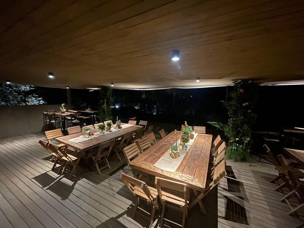 An outdoor wooden deck with multiple tables and chairs, some with plants.