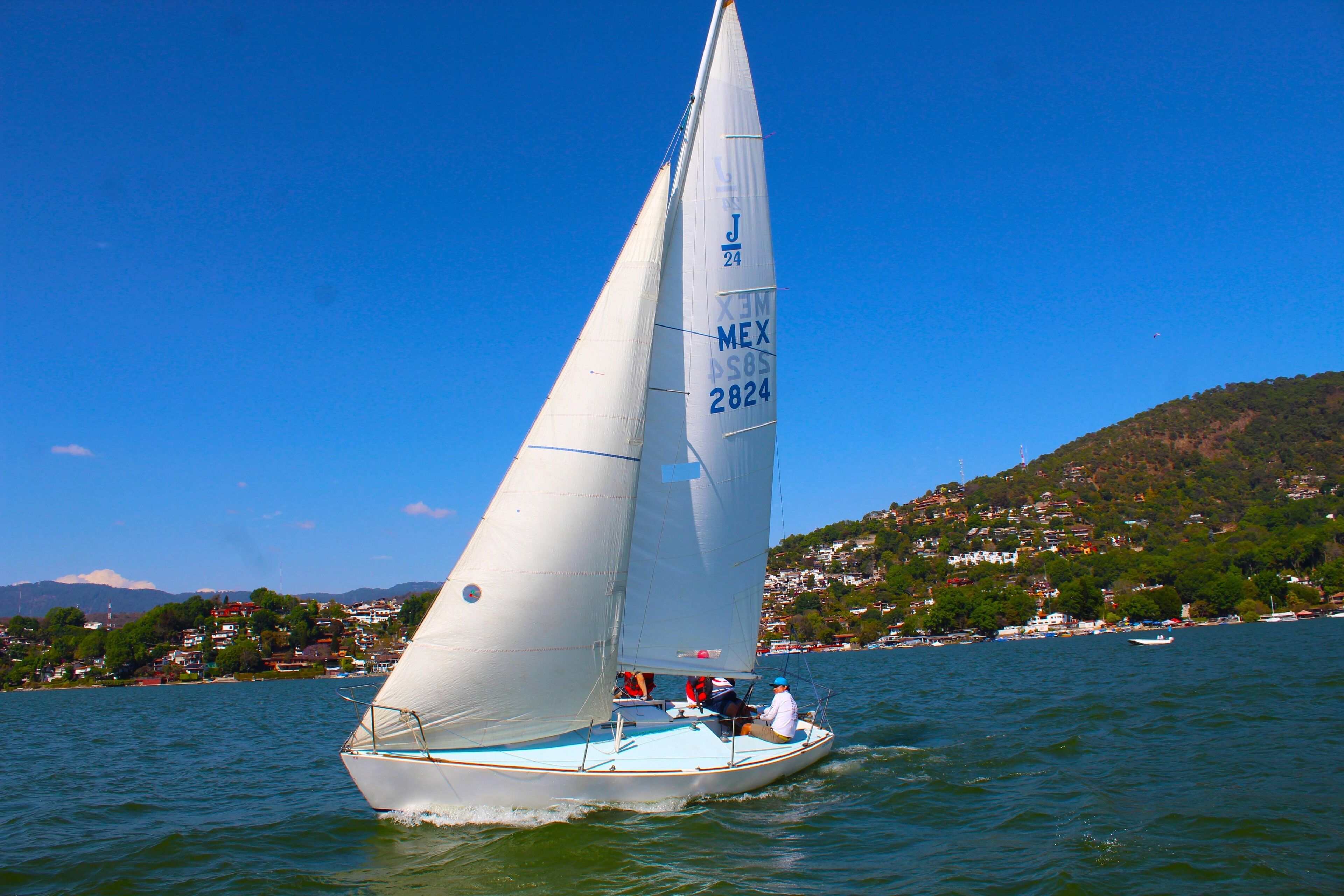 A sailboat with a white sail marked "J 24" and "MEX 2824" on the water.