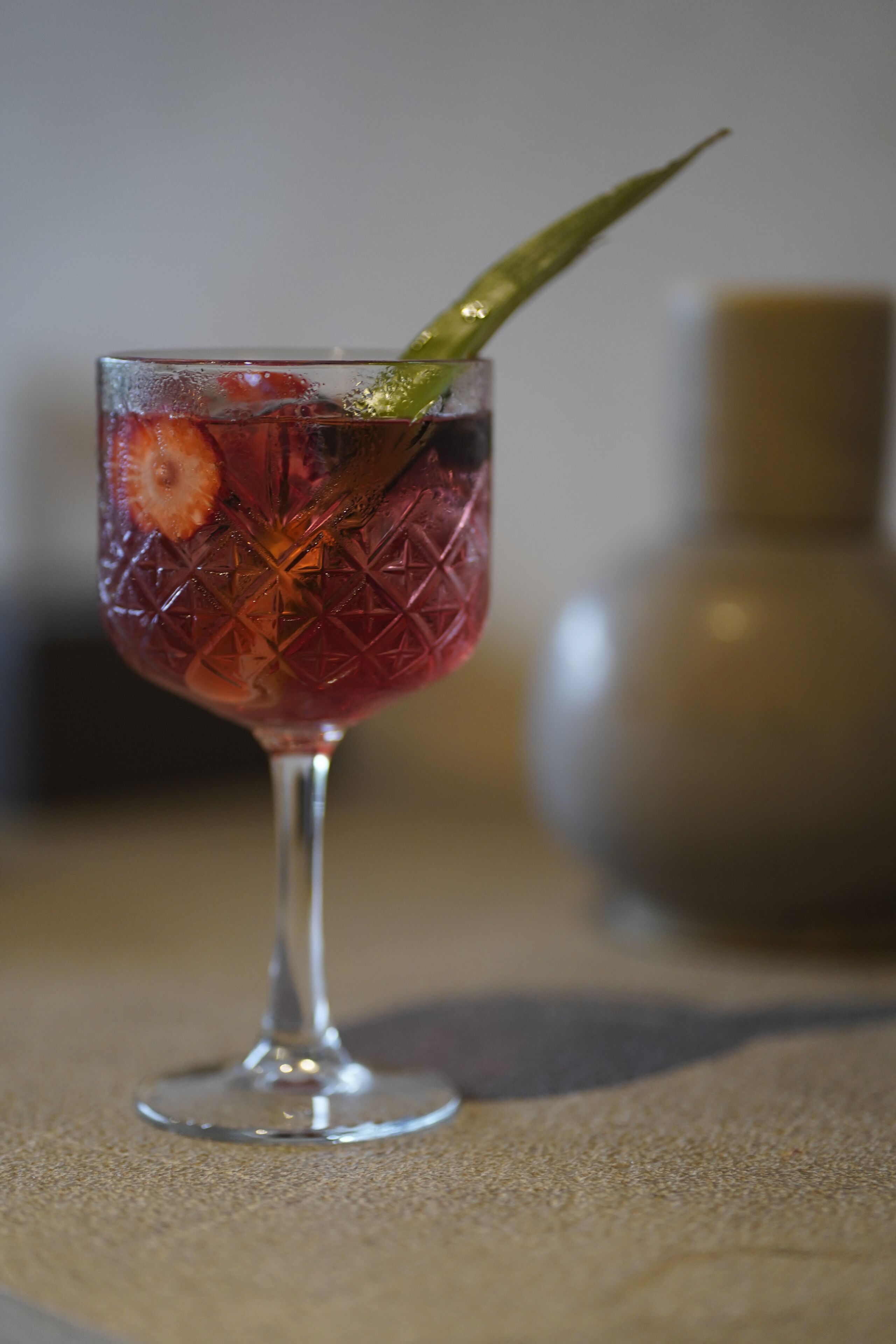 Un verre contenant une boisson, une fraise et une garniture verte, posé sur une table.
