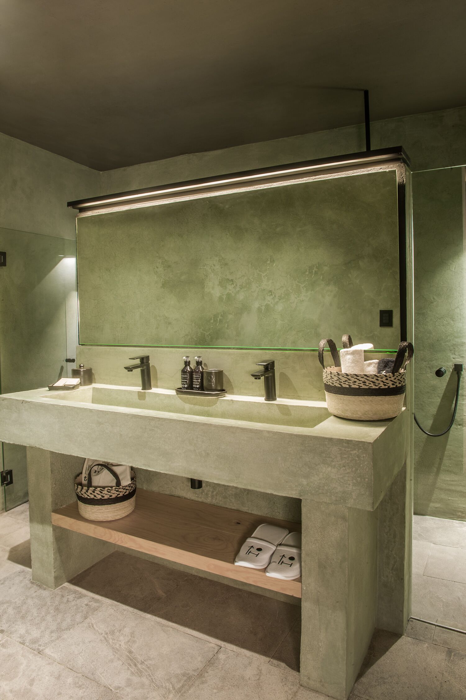 Une salle de bain avec un grand miroir, un lavabo double et une douche. On y trouve des serviettes et un panier sur le lavabo.