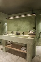 Une salle de bain avec un grand miroir, un lavabo double et une douche. On y trouve des serviettes et un panier sur le lavabo.