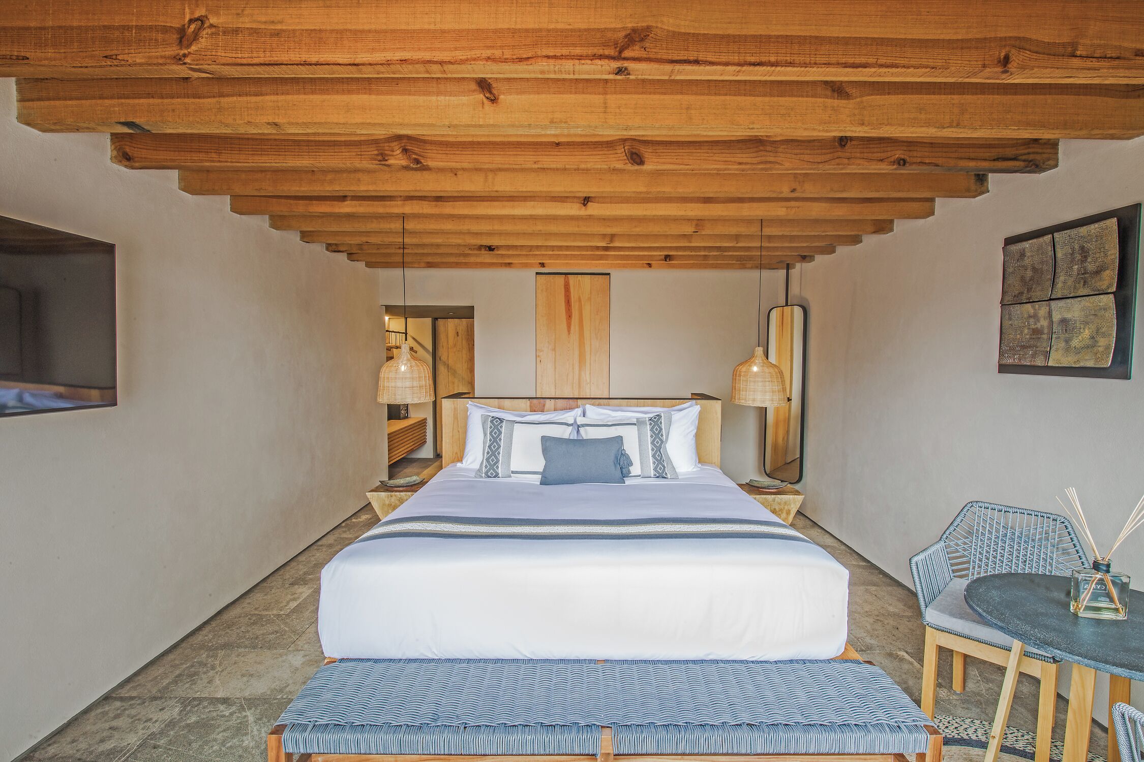 Ein Schlafzimmer mit einem großen Bett, einer Bank, einem Tisch und einem Sessel. An beiden Seiten des Bettes stehen Lampen.
