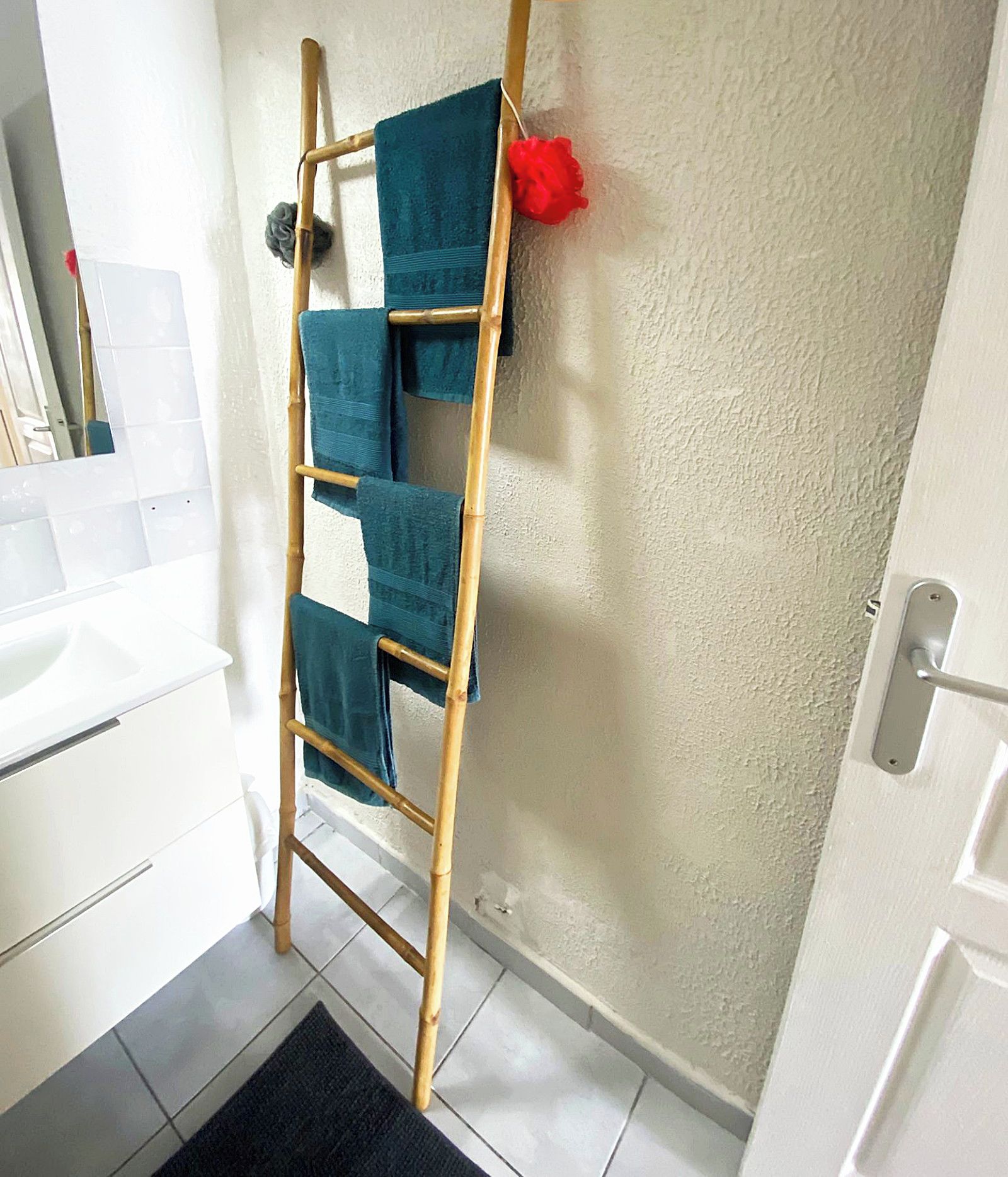 Um banheiro com escada de bambu para pendurar toalhas, pia branca e espelho.