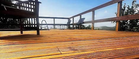A wooden deck with a view of the sea, a lounge chair, and a sunbed.