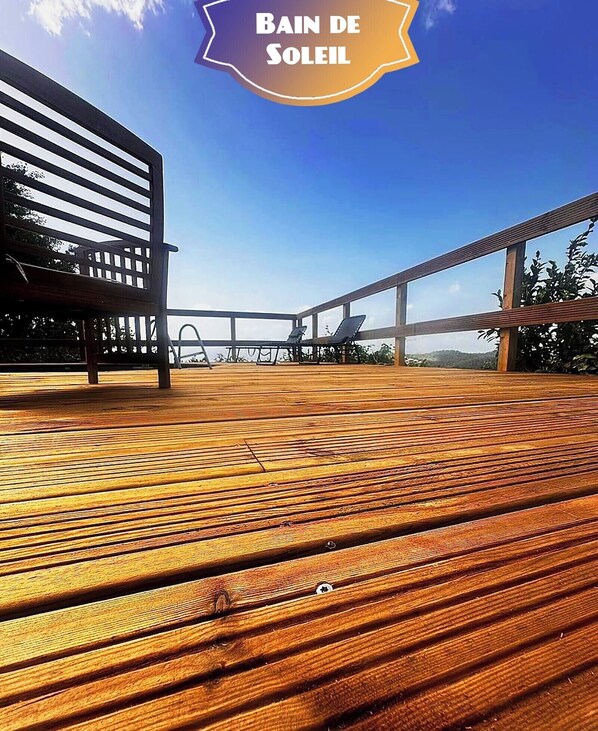 Una terraza de madera con vistas al mar, una silla de descanso y una cama para tomar el sol.