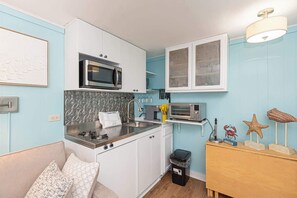 Une cuisine compacte avec des meubles blancs, un four à micro-ondes, un grille-pain et une petite poubelle.