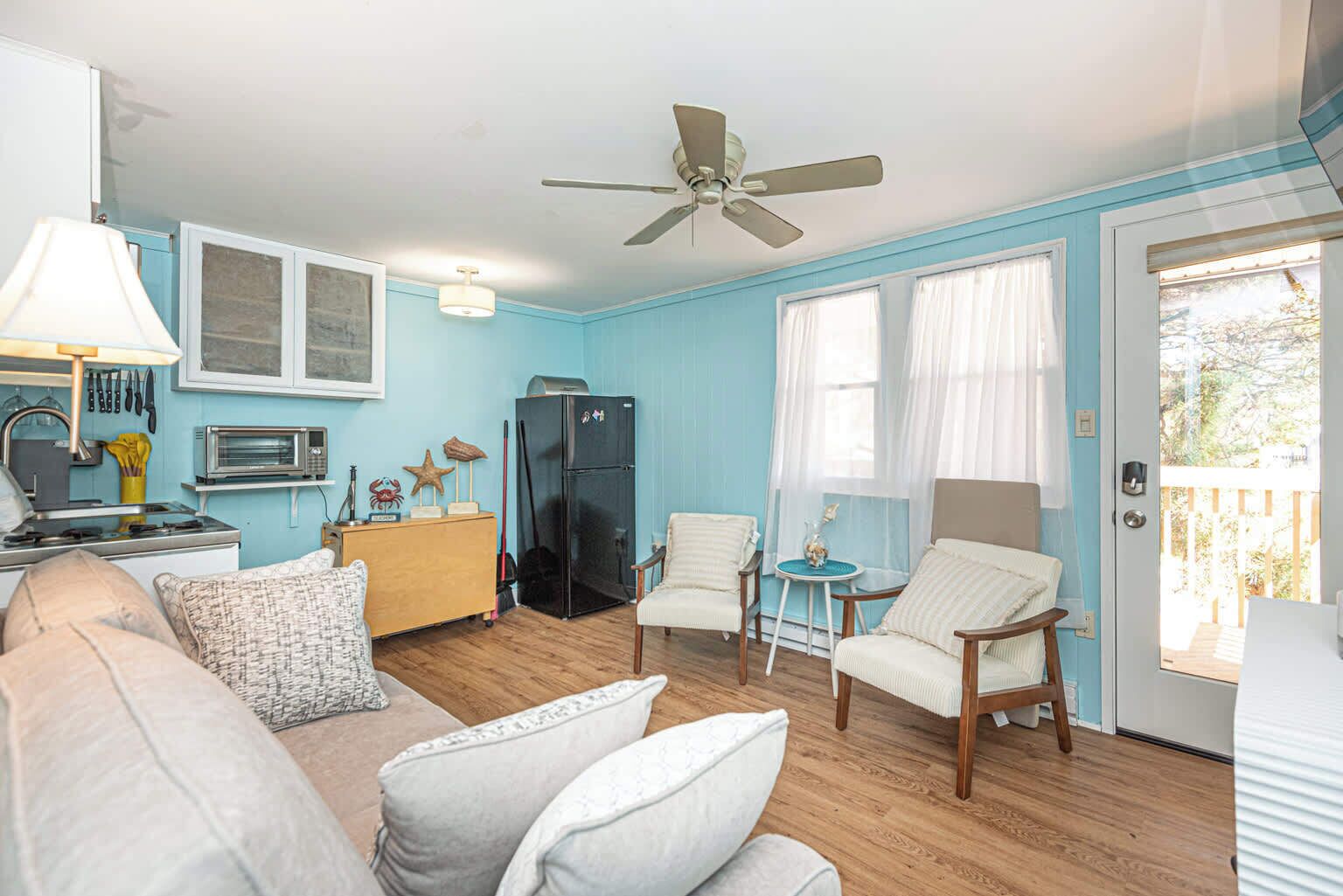 A compact living space with a kitchenette, a ceiling fan, and a door leading to an outdoor area.