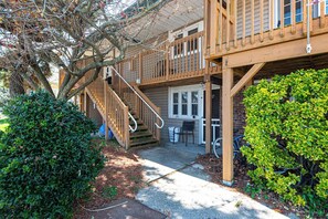 Une terrasse en bois avec un escalier menant à un espace abrité, un petit coin salon extérieur et une haie bien entretenue.
