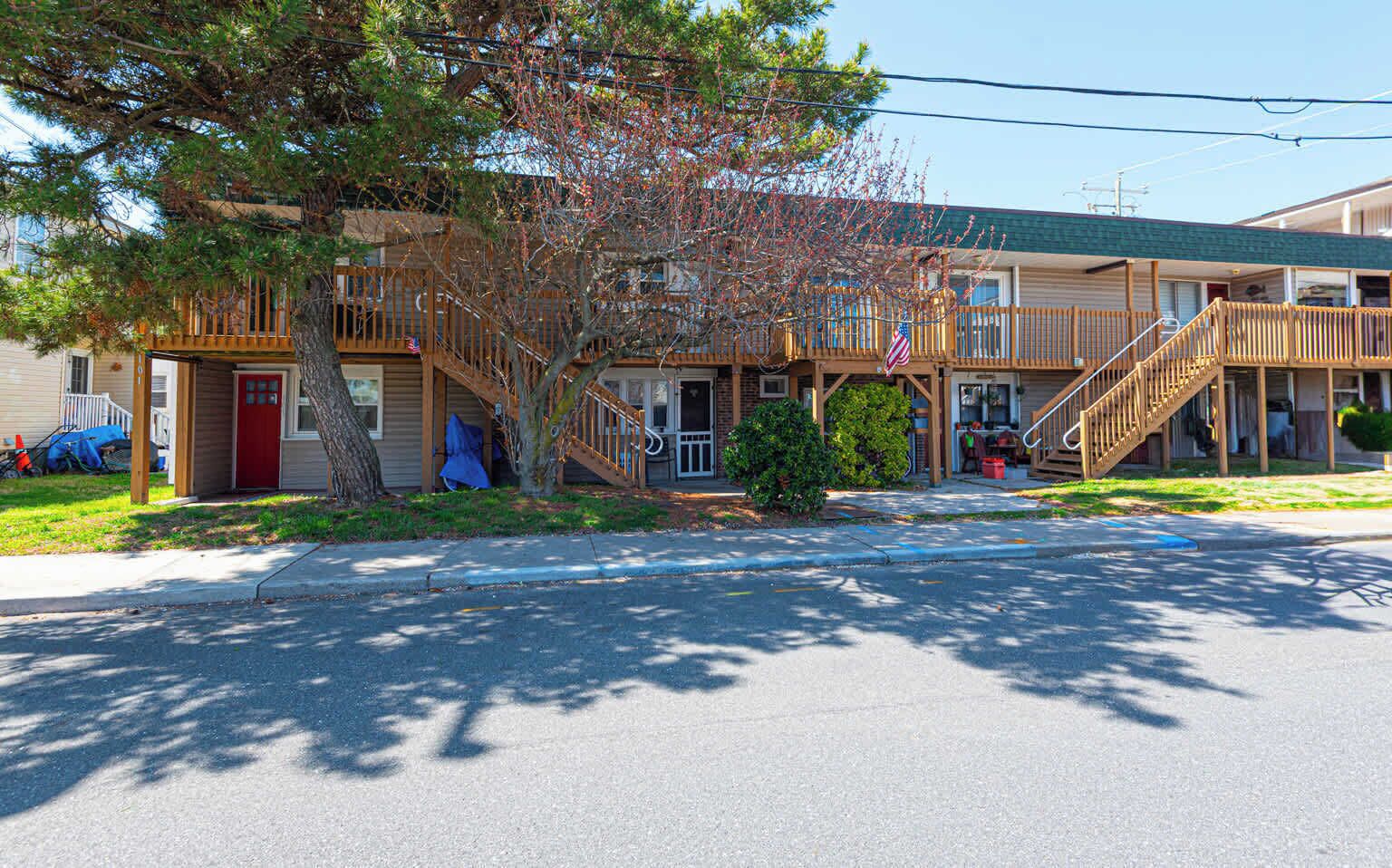 A motel with a covered outdoor seating area, a red door, and a staircase leading to the entrance.