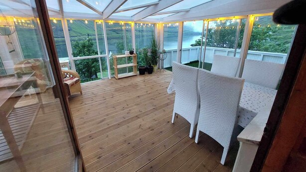 Une vaste terrasse dotée d’un plancher en bois, de sièges rembourrés blancs et d’un toit en verre offrant une vue sur l’extérieur.