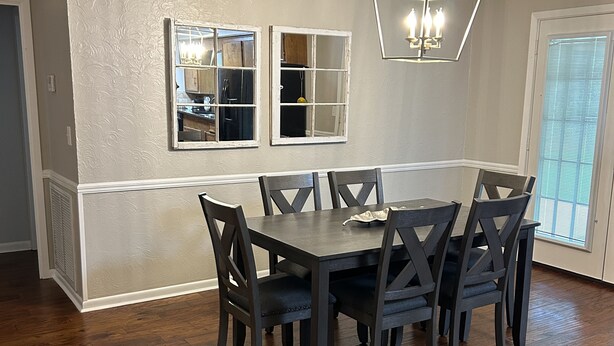 Un comedor con una mesa y sillas de madera oscura, una lámpara decorativa y una ventana con persianas.
