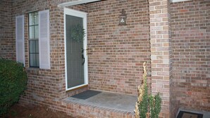 Una casa de ladrillo con una puerta blanca, un pequeño porche y una planta en maceta.