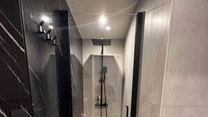 A modern bathroom with a glass-enclosed shower, a white towel on the floor, and a grey towel on the shelf.
