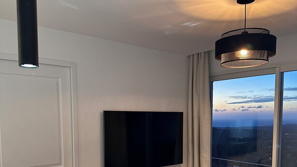 A modern dining area with a large TV, a dining table set with glasses and plates, a small round table, and a view of the city through large windows.