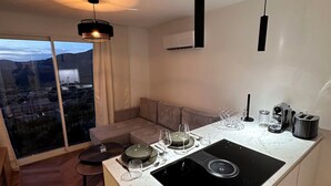 A modern kitchen with a central island, a dining area with a sofa, and a large window offering a city view.
