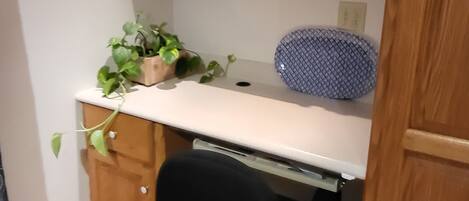 Un escritorio de madera con superficie blanca, una silla de oficina negra y un objeto azul estampado sobre el escritorio.