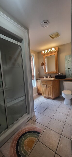 Ein Badezimmer mit Dusche, Toilette, Waschtisch und einem beleuchteten Spiegel.