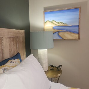 Ein Schlafzimmer mit einem Bett, einer Lampe, einem Gemälde und einem kleinen Tisch mit einer Vogel-Skulptur.