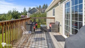 A deck with outdoor furniture, a covered area, and a house with large windows. - Fleur de Lis 4bed 3bath & Mountain Views (Wasilla)