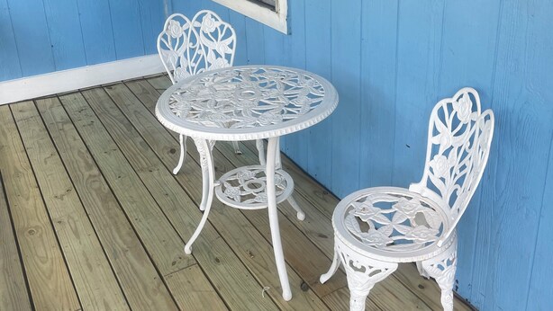 A blue-painted porch with two white metal chairs and a table, a window with blinds, and a floral wreath on the wall. - Blue Pool House  (Lone Oak)