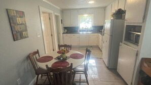 A compact kitchen with white cabinets, a dining table with chairs, and a microwave. - Blue Pool House  (Lone Oak)