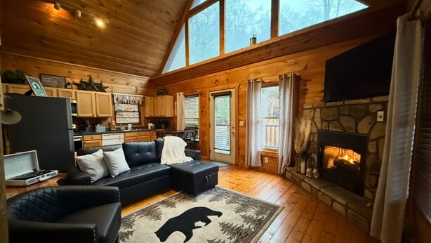 Interior acolhedor de uma cabana com lareira, piso de madeira, sofá de couro preto e um tapete de pele de urso.