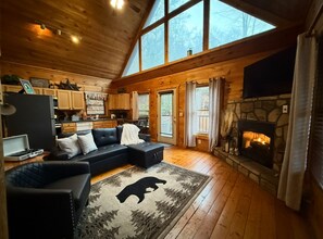 Ein gemütliches Blockhaus-Interieur mit Kamin, Holzböden, einer schwarzen Ledersofa und einem Bärenfellteppich.