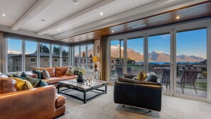 A spacious living room with leather sofas, a coffee table, and large windows offering mountain views. - The Ballarat Apartment (Queenstown)