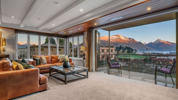A spacious living room with a leather sofa, a coffee table, and a view of mountains through large windows. - The Ballarat Apartment (Queenstown)