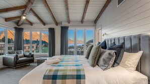 A bedroom with a large bed, a sofa, and a view of mountains through large windows. - The Ballarat Apartment (Queenstown)