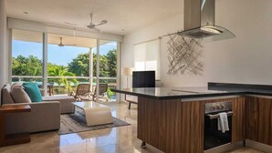 A modern kitchen with a central island, a built-in oven, and a large window overlooking a green landscape. - Tranquility Base - Golf and Beach Resort (Akumal)