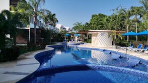 A swimming pool with a tiled edge, surrounded by lounge chairs and umbrellas, with palm trees and a building in the background. - Tranquility Base - Golf and Beach Resort (Akumal)
