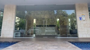 A modern building entrance with glass doors, a tiled floor, and a sign indicating a parking area. - Tranquility Base - Golf and Beach Resort (Akumal)