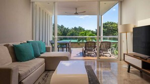 A modern living room with a sofa, chairs, a flat-screen TV, and a balcony with a view of greenery. - Tranquility Base - Golf and Beach Resort (Akumal)