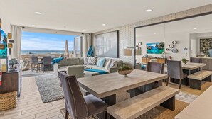 Una sala de estar moderna con televisor grande, asientos cómodos, comedor y vista al océano.