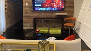 Un salon moderne doté d’un grand téléviseur à écran plat fixé à un mur en briques, d’une table basse en verre agrémentée d’objets décoratifs, d’un canapé confortable et d’une cheminée.