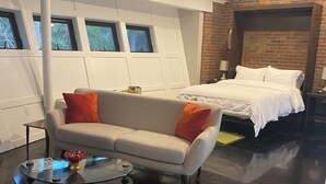 Une chambre moderne avec un canapé, une table basse en verre, un lit avec une literie blanche et un mur d’accent en briques.