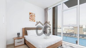 Quarto moderno com uma cama grande, mesa de cabeceira, relógio de parede e vista para uma piscina.