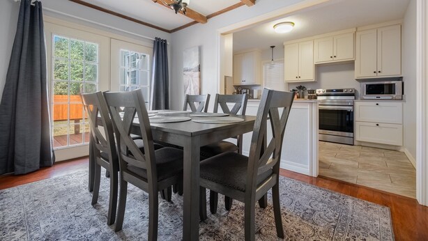 A dining area with a dark wooden table and chairs, a patterned rug, and a view of a kitchen with white cabinets and appliances. - Cozy two bedroom home in Amarillo. Pet Friendly! (Amarillo)
